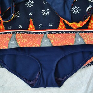 May include: A two-piece swimsuit with a navy blue bottom and a top. The top has a navy blue background and a pattern of white, orange, and yellow shapes. The top has a wrap-around design.