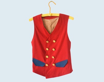 May include: A red vest with gold buttons and blue pocket accents hangs on a yellow hanger. The vest has a V-neck and a tan lining. This vintage-style garment is suitable for costumes or everyday wear.
