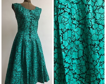 May include: A vintage green and black floral print dress with a fitted bodice and a full skirt. The dress has a round neckline and short sleeves.