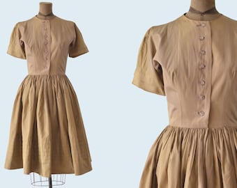 May include: A brown vintage dress with a button-up front and short sleeves. The dress has a full skirt and is made of a lightweight fabric.