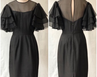 May include: A black dress with a sheer, ruffled overlay on the sleeves. The dress has a fitted bodice and a straight skirt.