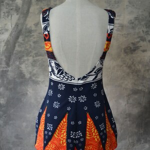 May include: A sleeveless dress with a low back, displayed on a mannequin. The dress has a navy blue base with white, orange, and yellow geometric patterns. The straps and upper back have a contrasting pattern. The hemline features orange and yellow leaf shapes.