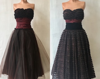 May include: Two strapless vintage dresses with a brown tulle skirt and a burgundy bodice. One dress has a velvet sash and the other has a ruffled skirt.