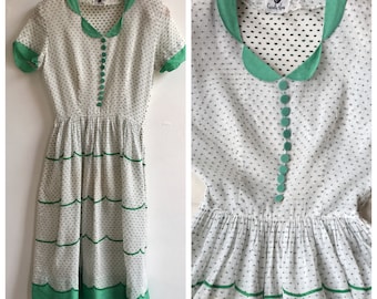 May include: A white dress with green polka dots and trim. The dress has a Peter Pan collar, short sleeves, and a full skirt. The dress is made of a lightweight fabric and has a vintage look.