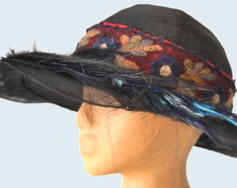 May include: A black wide-brimmed hat with a red, blue, and brown embroidered band and blue feathers.