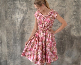 Könnte beinhalten: Eine Frau trägt ein rosa-braunes Blumenkleid mit weißem Kragen und kurzen Ärmeln. Das Kleid hat ein tailliertes Oberteil und einen vollen Rock.