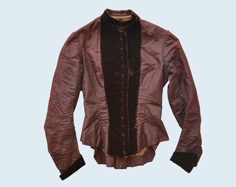 May include: A brown jacket with a black velvet trim down the front. The jacket has a high collar and long sleeves.