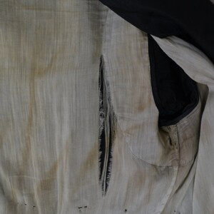 May include: The inside of a garment with a large tear in the fabric. The fabric is a light beige color and the tear is a dark black color. The garment is made of a thin, woven fabric.