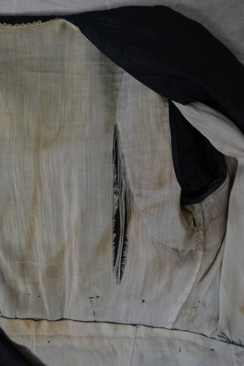May include: The inside of a garment with a large tear in the fabric. The fabric is a light beige color and the tear is a dark black color. The garment is made of a thin, woven fabric.