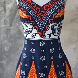 May include: A sleeveless dress with a V-neck, in navy blue with orange, white, and yellow geometric patterns. The dress has a fitted bodice and a flared skirt, showcasing a vintage style.