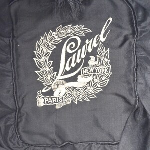 Pode incluir: Um chap&eacute;u de tecido preto com um logotipo Laurel bordado em branco. O logotipo apresenta uma coroa com as palavras "Laurel", "Nova Iorque" e "Paris".
