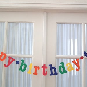 May include: A colorful banner with the words "happy birthday jack" in rainbow colors. The banner is strung across a window.