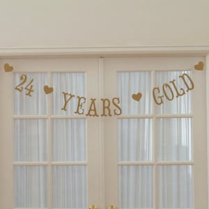 May include: Gold banner with hearts and the text "24 YEARS GOLD" hanging on a white door.