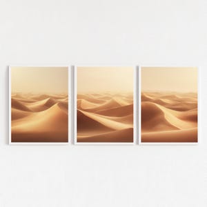 Könnte beinhalten: Drei gerahmte Drucke mit einer Wüstenlandschaft mit rollenden Sanddünen. Die Dünen haben eine warme, goldene Farbe, und der Himmel ist ein weiches, dunstiges Beige. Die Drucke werden vor einem weißen Hintergrund präsentiert.
