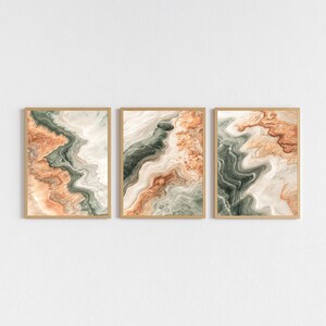 Puede incluir: Conjunto de tres impresiones artísticas abstractas enmarcadas. Cada impresión presenta un diseño fluido con colores naranja, verde y blanco, que recuerda a la piedra natural. Los marcos son de color marrón claro.