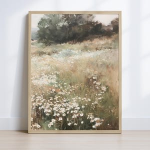 Op de afbeelding: Een ingelijst landschapsschilderij met een veld witte wilde bloemen. Het kunstwerk heeft een zacht kleurenpalet van groen, bruin en wit, met een vage achtergrond van bomen en een lichte lucht. De lijst is licht van kleur.