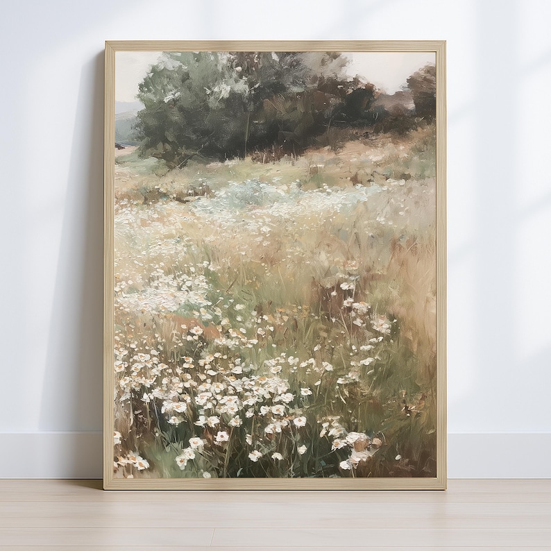 Op de afbeelding: Een ingelijst landschapsschilderij met een veld witte wilde bloemen. Het kunstwerk heeft een zacht kleurenpalet van groen, bruin en wit, met een vage achtergrond van bomen en een lichte lucht. De lijst is licht van kleur.