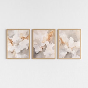 May include: A triptych of framed abstract art prints. Each print displays a watercolour design with flowing shapes in white, beige, and brown hues. The frames are light wood, creating a modern and minimalist aesthetic. The artwork is suitable for various interior styles.