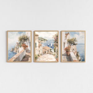 Könnte beinhalten: Set aus drei gerahmten Aquarelldrucken mit Küstenmotiven. Jeder Druck zeigt eine andere Ansicht einer Küstenstadt mit Gebäuden, Gehwegen und Meerblick. Das Kunstwerk ist in einer weichen, gedämpften Farbpalette gehalten.