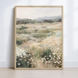 Op de afbeelding: Een ingelijst landschapsschilderij toont een veld met witte wilde bloemen in een weide. Het kunstwerk toont een pad dat door het veld leidt, met glooiende heuvels en een gedempte lucht op de achtergrond. De schildering zit in een lichte houten lijst.
