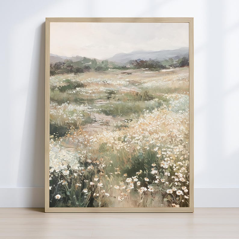 Op de afbeelding: Een ingelijst landschapsschilderij toont een veld met witte wilde bloemen in een weide. Het kunstwerk toont een pad dat door het veld leidt, met glooiende heuvels en een gedempte lucht op de achtergrond. De schildering zit in een lichte houten lijst.