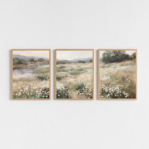 Può includere: Tre stampe artistiche di paesaggi incorniciate. Ogni stampa presenta una serena scena di prato con un fiume, fiori selvatici e dolci colline. L'opera d'arte è in tenui tonalità di verde, beige e marrone, con una cornice in legno chiaro.