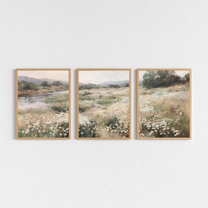Op de afbeelding: Drie ingelijste landschapskunstafdrukken. Elke afdruk toont een serene weidesc&egrave;ne met een rivier, wilde bloemen en glooiende heuvels. Het kunstwerk is in zachte, gedempte tinten groen, beige en bruin, met een licht houten frame.