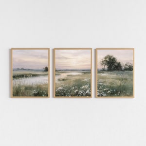 May include: Set of three framed landscape art prints. Each print features a serene marsh scene with a river, tall grasses, and a soft, pastel color palette of greens, pinks, and creams. The frames are a light wood color.