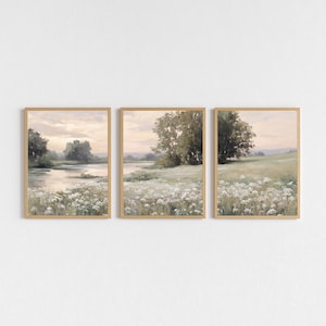 May include: Set of three framed landscape art prints. Each print features a serene landscape with a river, trees, and a field of white flowers. The color palette includes soft greens, beige, and muted tones, creating a calming aesthetic.