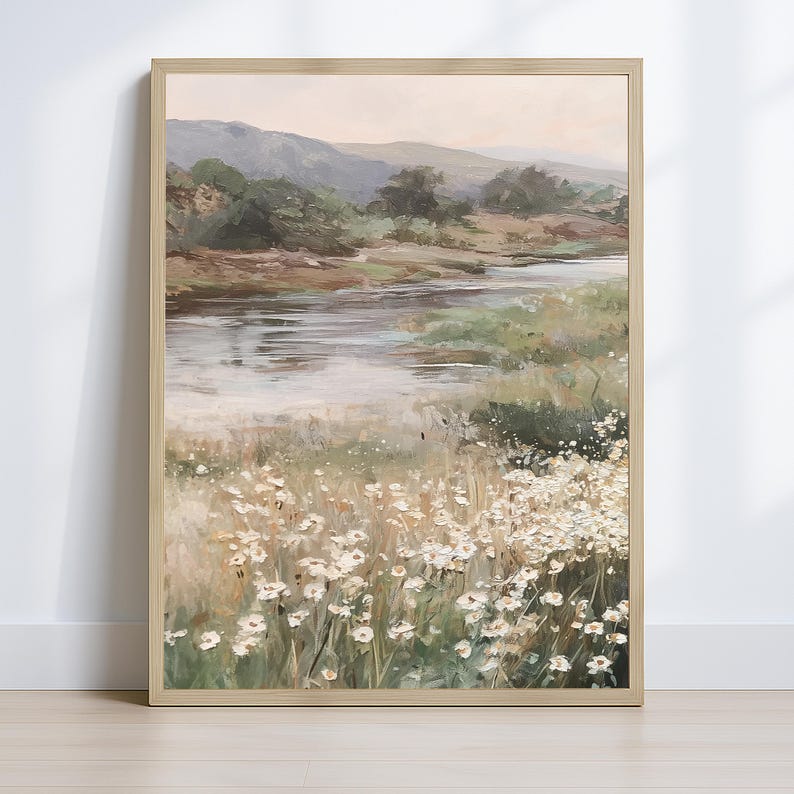 Op de afbeelding: Een ingelijst landschapsschilderij dat een serene riviersc&egrave;ne uitbeeldt. Het kunstwerk toont een rivier die door een vallei stroomt, met bergen op de achtergrond. Witte wilde bloemen bloeien op de voorgrond en geven een vleugje helderheid.
