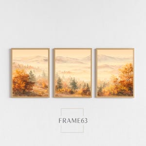 Pode incluir: Três impressões de arte emolduradas de paisagens. Cada impressão retrata uma cena de montanha nebulosa com árvores em tons de laranja, amarelo e verde. O texto "FRAME63" está centralizado abaixo das molduras.