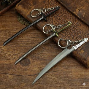 Puede incluir: Tres llaveros de espada en miniatura. Uno es negro con detalles rojos, otro tiene un mango verde y dorado, y el tercero es plateado con un mango blanco. Cada llavero tiene un anillo y una cadena de metal.