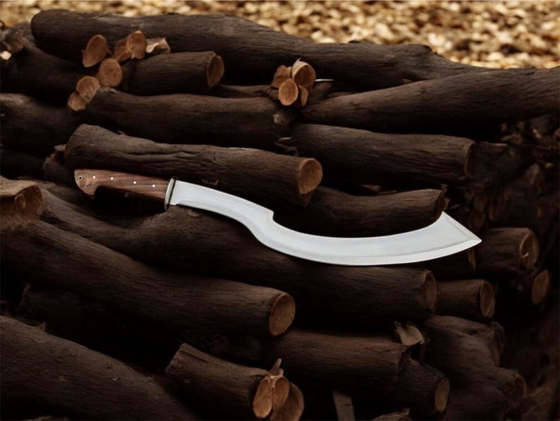 May include: A large, curved blade knife with a wooden handle and a silver-colored blade. The knife is resting on a pile of dark brown logs. The handle is a light brown color.