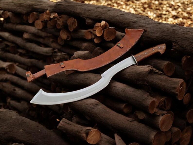 May include: A curved, silver-bladed knife with a wooden handle and a brown leather sheath. The knife is lying on a pile of cut logs. The sheath has a strap and buckle closure.