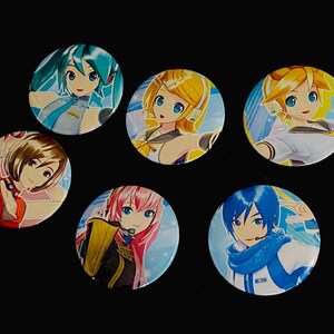 Op de afbeelding: Een verzameling van zes ronde anime-personagebuttons. Elke button toont een ander personage met levendige haarkleuren, waaronder blauw, geel, roze en bruin. De buttons liggen op een zwarte achtergrond.