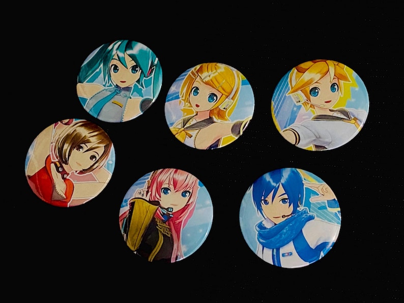 Op de afbeelding: Een verzameling van zes ronde anime-personagebuttons. Elke button toont een ander personage met levendige haarkleuren, waaronder blauw, geel, roze en bruin. De buttons liggen op een zwarte achtergrond.