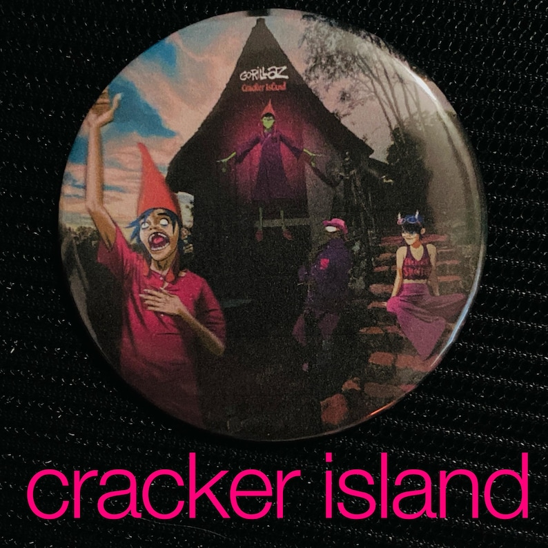 May include: A round button featuring the Gorillaz band's "Cracker Island" album art. The design includes cartoon figures in a surreal setting with a red-hatted character in the foreground. The text "cracker island" is displayed in pink.