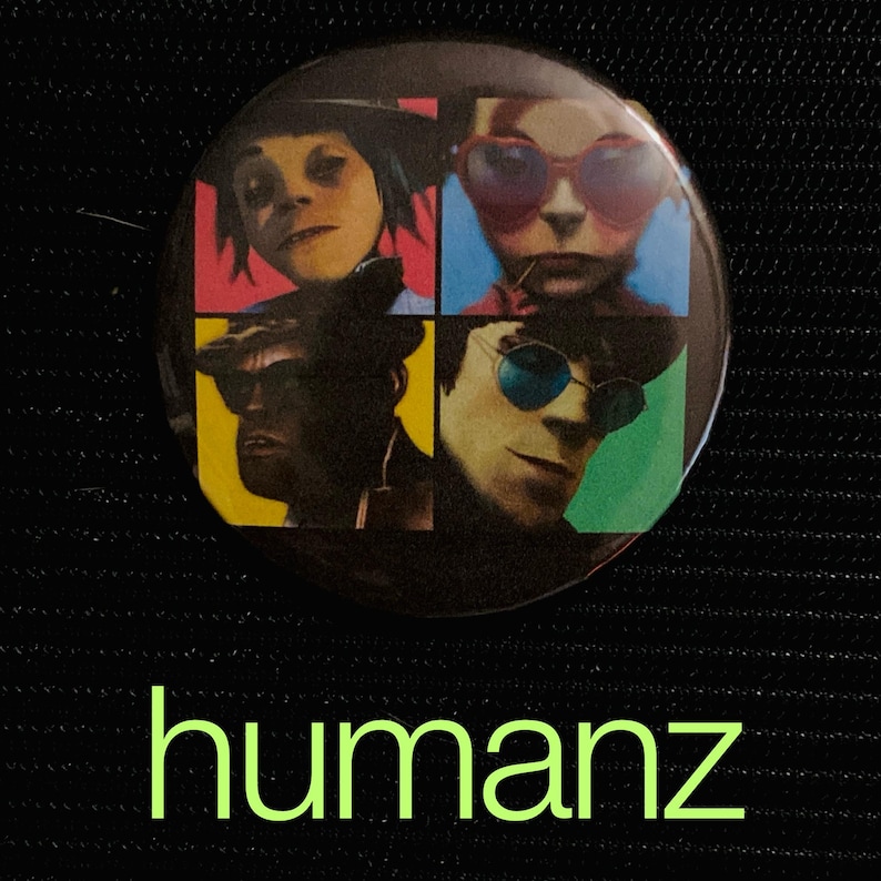 May include: A round button featuring four colorful squares, each with a different cartoon character portrait. The button has the word "humanz" in a neon green font at the bottom. The background is black.