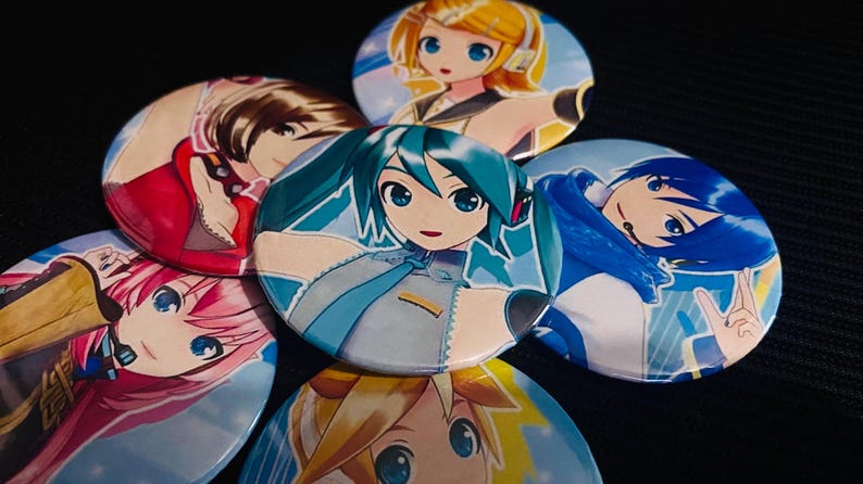 Op de afbeelding: Een verzameling ronde anime-personagebuttons. De buttons tonen kleurrijke illustraties van anime-personages met grote ogen en verschillende haarkleuren, waaronder blauw, geel, roze en bruin. De buttons zijn gerangschikt op een donkere ondergrond.