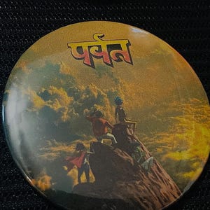 May include: Round button with a golden yellow background featuring an illustration of people on a mountain. The button has the word "पर्वत" in red letters at the top. The image has a vintage, adventure theme.