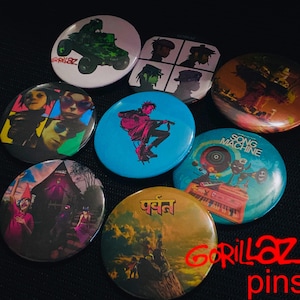 May include: A collection of Gorillaz pins featuring various designs. The pins showcase images of the band members, album art, and other graphics. The pins are round and have a glossy finish, with a variety of colors and styles.