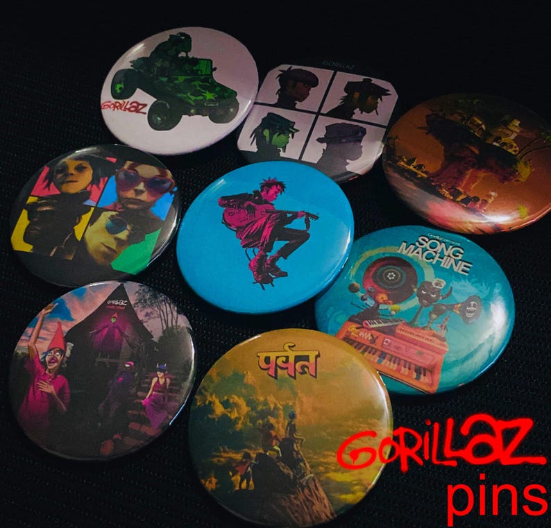 May include: A collection of Gorillaz pins featuring various designs. The pins showcase images of the band members, album art, and other graphics. The pins are round and have a glossy finish, with a variety of colors and styles.