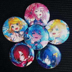 May include: A collection of six round anime-style character buttons. Each button features a different character with vibrant hair colors, including pink, yellow, blue, and red. The characters are depicted with detailed facial features and colorful outfits.