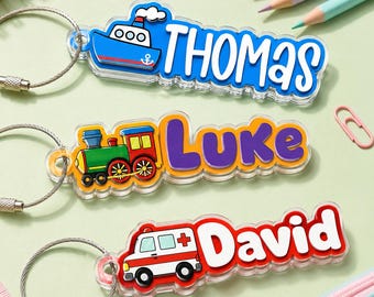May include: Three acrylic keychains with metal wire loops. The first features a blue boat and the name Thomas in white. The second shows a green and red train with the name Luke in purple. The third displays a white and red ambulance with the name David in red.