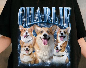 May include: Black t-shirt featuring a graphic of five Corgi dogs with the name "CHARLIE" in a blue, lightning-themed font. The dogs are in various poses, with some showing their tongues. The shirt is a crew neck.
