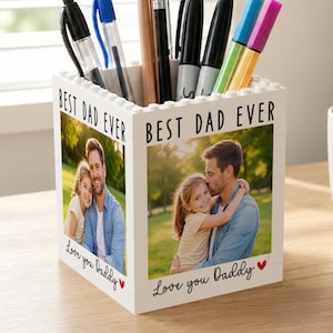 May include: A white desk organizer with the text "BEST DAD EVER" and photos of a father and child. The organizer is filled with pens, pencils, and markers. The words "Love you Daddy" are written below the photos.