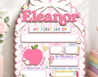 May include: A pink and white striped scalloped sign featuring the name Eleanor in large pink letters, topped with a white bow. The board includes sections for My First Day Of, date, height, teacher, things I love, and what I want to be.
