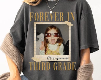 May include: A charcoal gray t-shirt featuring a vintage-style photo frame graphic. The text reads FOREVER IN THIRD GRADE with Mrs. Amanda printed below the photo. The photo shows a child wearing sunglasses and making a peace sign with their hand.