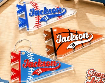 May include: Three triangular pennant-shaped keychains made of clear acrylic. Each features a sports ball graphic, the name Jackson in script, and the number 35. One is white with a baseball, one is orange with a basketball, and one is blue with a baseball.