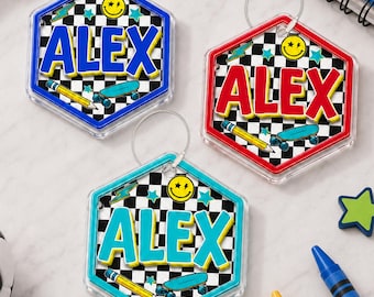 May include: Three hexagonal acrylic keychains featuring a black and white checkered background. Each keychain displays the name ALEX in bold letters, a yellow smiley face, a blue skateboard, a yellow pencil, and small teal star icons.